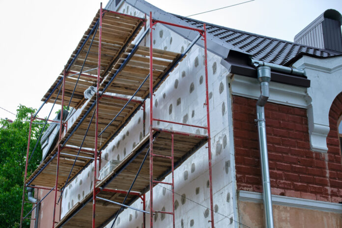 Building facade under renovation works with construction scaffolding frame. Wall insulation with styrofoam sheets for energy efficient home